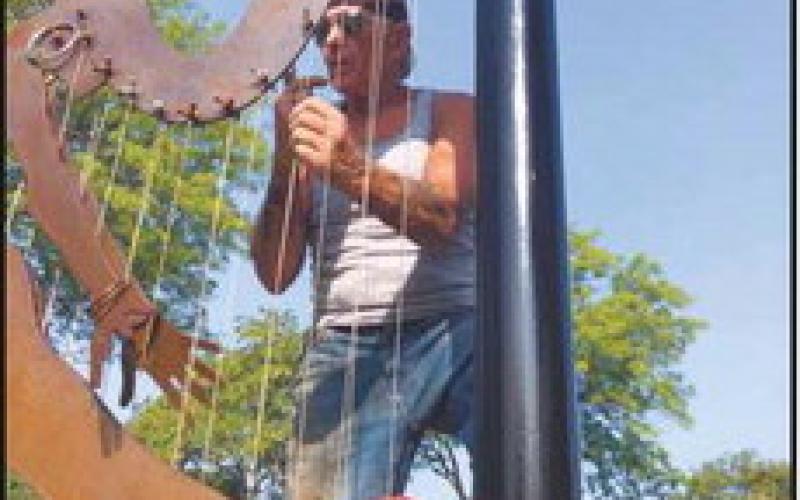 At left, “Cactus Dancer” leaves the exhibit lineup. Mike Sohikian prepares the sculpture to be lifted and loaded as part of the removal process. Above, Mr. Sohikian attaches the strings and wind chimes to his sculpture “Harp.”
