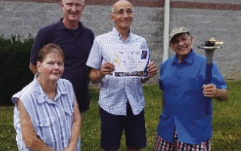 Several Peace Runners with their banner in 2024. Former Mayor Tom Mackin and members of the community in 2024 holding the Peace Torch.