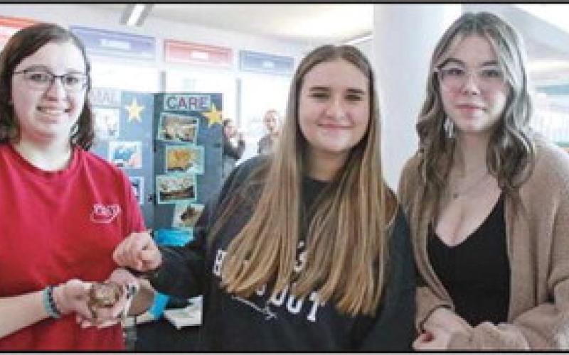 Mia Dommer, a senior from Otsego schools, holds a spiny-tailed agama for eighthgrade students Senna Musa and Audrey Smith to pet. Small animal care is among the most visited areas of the expo.