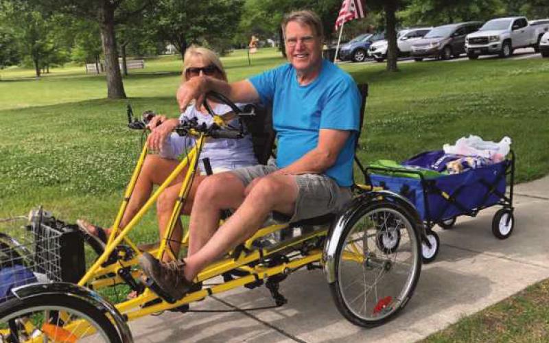 Charlie Gries, founder and coordinator of Perrysburg Slow Rollers, and partner Cathy Gries heading to Wednesday at Woodlands lunchtime concert series with a cart full of food to serve free hotdog lunches to audience members.