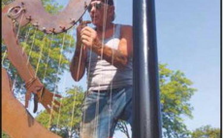 At left, “Cactus Dancer” leaves the exhibit lineup. Mike Sohikian prepares the sculpture to be lifted and loaded as part of the removal process. Above, Mr. Sohikian attaches the strings and wind chimes to his sculpture “Harp.”