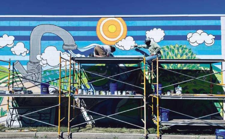 Above is the mural painting in process by artist Terry A. Burton and his team. Mr. Burton is pictured at right. Below is the completed masterpiece at the ribbon-cutting ceremony with, from left: Doug Williams, Maren Tregillis, Amy Siders, Scott Williams, Julie Williams and Jessica Jacobs.